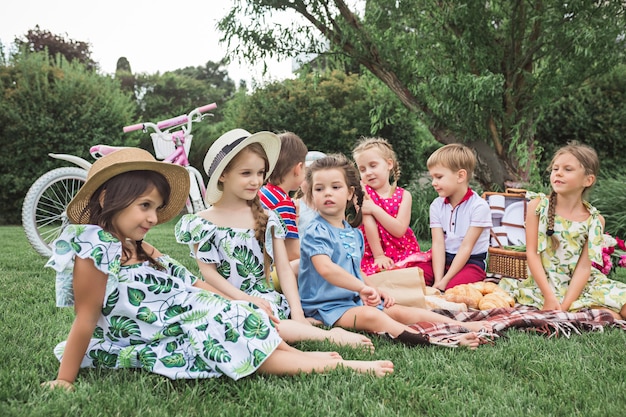 Bezpłatne zdjęcie koncepcja mody dla dzieci. grupa nastolatków chłopców i dziewcząt siedzących na zielonej trawie w parku.