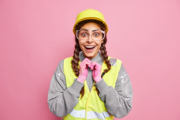 Koncepcja naprawy. Pozytywna kobieta mechanik nosi jednolity budynek inżynierii wygląda szczęśliwie na białym tle nad różową ścianą. Budownictwo inżynieryjne i przemysłowe. Robotnik w odzieży roboczej