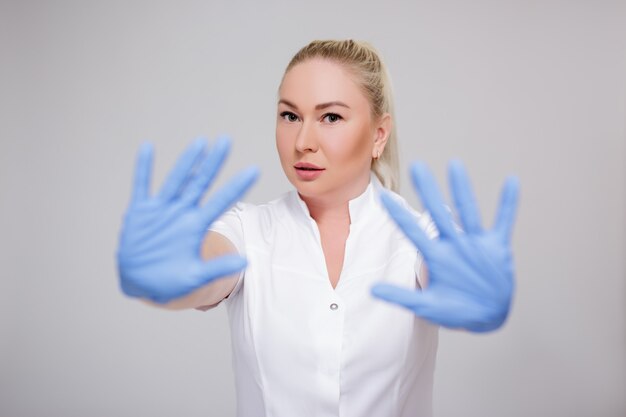 Koncepcja opieki zdrowotnej i pandemii wirusa koronowego - portret lekarki w białym mundurze i niebieskich rękawiczkach pokazujących znak stopu na szarym tle
