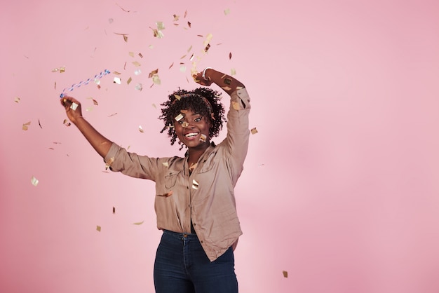 Bezpłatne zdjęcie koncepcja partii. rzucanie konfetti w powietrze. amerykanin afrykańskiego pochodzenia kobieta z różowym tłem behind