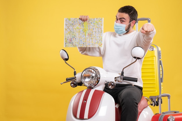 Koncepcja podróży z dumnym facetem w masce medycznej siedzącej na motocyklu z żółtą walizką na nim i pokazującym mapę na żółto