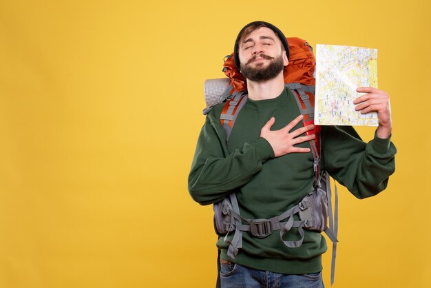 Koncepcja podróży z marzycielskim młodym facetem z paczką i trzymającą mapą położyła dłoń na jego sercu na żółto