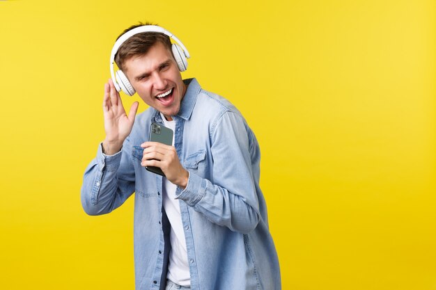 Koncepcja reklamy czasu wolnego, technologii i aplikacji. Przystojny młody mężczyzna rasy kaukaskiej zabawy, grając aplikację karaoke na telefonie komórkowym, używając smartfona jako mikrofonu i śpiewając ze słuchawkami.