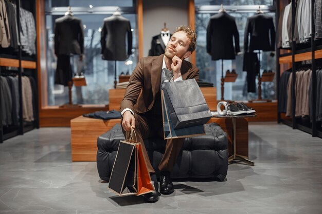 Koncepcja sprzedaży, zakupów, mody, stylu i ludzi. Elegancki młody człowiek wybierając obuwie w centrum handlowym.