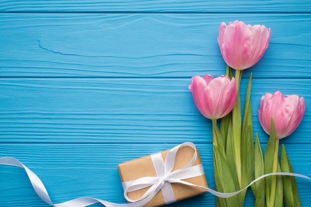 Koncepcja szczęśliwy międzynarodowy dzień kobiet. górne nad płaskim leżące nad głową zdjęcie pięknych tulipanów na zielonych łodygach i owinięte w papier pakowy wstążka na białym tle jasny niebieski stół z pustą przestrzenią