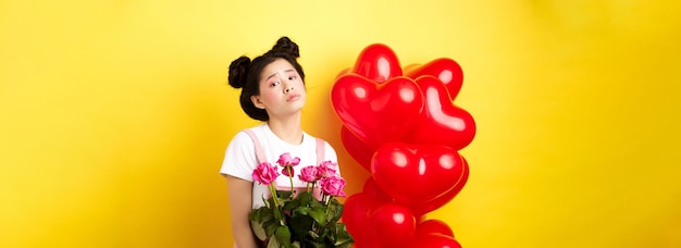Bezpłatne zdjęcie koncepcja szczęśliwych walentynek smutna i ponura azjatycka kobieta trzymająca bukiet róż i zdenerwowana i l