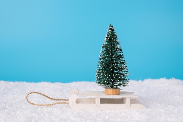 Koncepcja wesołych świąt. zbliżenie zdjęcie małej zabawki choinki stojącej na drewnianych sankach retro w śniegu i niebieskim jasnym tle nieba