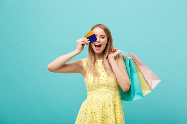 Koncepcja zakupów i stylu życia: Piękna młoda dziewczyna z kartą kredytową i kolorowymi torbami na zakupy. Na białym tle na niebieskim tle.