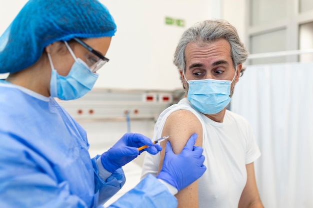 Koncepcja zapobiegania chorobom związanym ze szczepieniami Mężczyzna w medycznej masce na twarz otrzymujący w szpitalu szczepionkę przeciw Covid19 lub grypę Profesjonalna pielęgniarka lub lekarz podający pacjentowi zastrzyk przeciwwirusowy