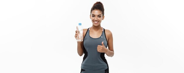 Koncepcja zdrowego i fitness piękna African American girl w ubrania sportowe trzymając plastikową butelkę wody po treningu izolowany na białym tle studio