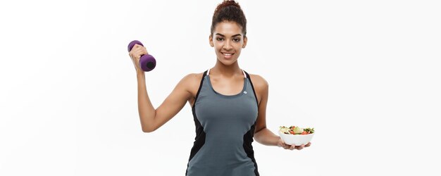 Koncepcja zdrowego i fitness piękny sportowy Afroamerykanin na diecie trzymając hantle i świeże sa
