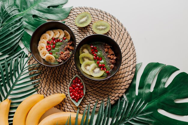 Koncepcja zdrowej żywności. Widok z góry na stół z miskami do smoothie. Talerz zwieńczony kiwi, granola, granat, chia, awokado.