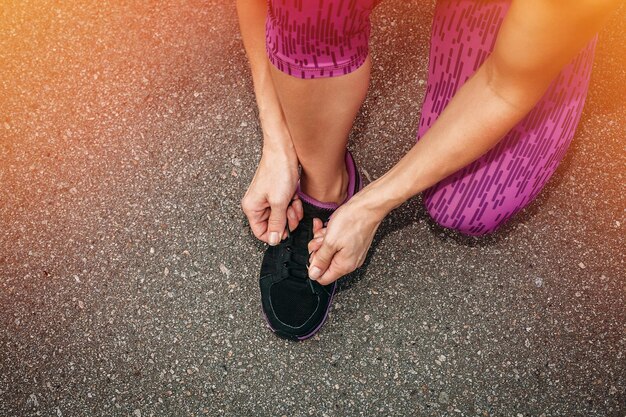 Koncepcja zdrowia, ludzi, sportu i stylu życia - buty do biegania - zbliżenie kobiety wiązania sznurowadeł. kobieta fitness biegacz przygotowuje się do biegania na świeżym powietrzu. czerwone podświetlenie na tle