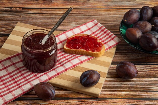 Konfitura śliwkowa w szklanym słoju i na grzance na ręczniku kuchennym w kratkę.