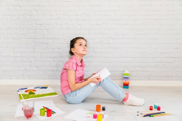 Kontemplujący dziewczyny obsiadanie na podłogowym rysunku na białym papierze z barwionym ołówkiem