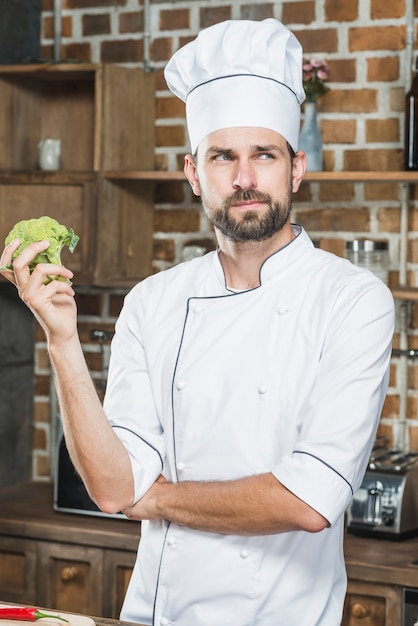 Bezpłatne zdjęcie kontemplujący męski szef kuchni trzyma zielonych organicznie brokuły w jego ręce