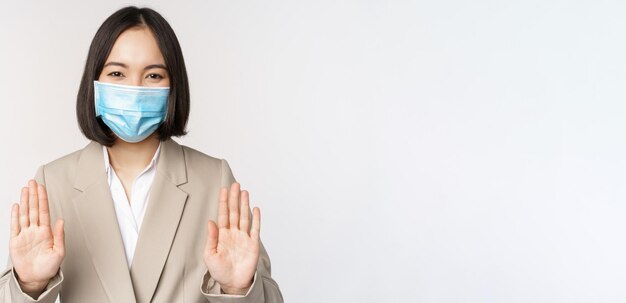Koronawirus i koncepcja pracy Portret azjatyckiej kobiety biurowej kobiety w miejscu pracy noszącej medyczną maskę na twarz i pokazującej gest zakazu zatrzymania na białym tle