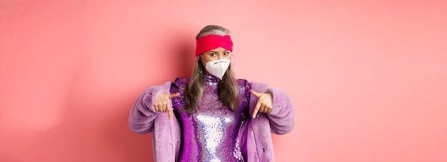 Bezpłatne zdjęcie koronawirus i koncepcja zakupów stylowa azjatycka starsza kobieta w fioletowych ubraniach i masce wskazującej na twarz