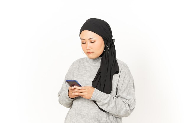 Korzystanie ze smartfona pięknej azjatyckiej kobiety noszącej hidżab na białym tle