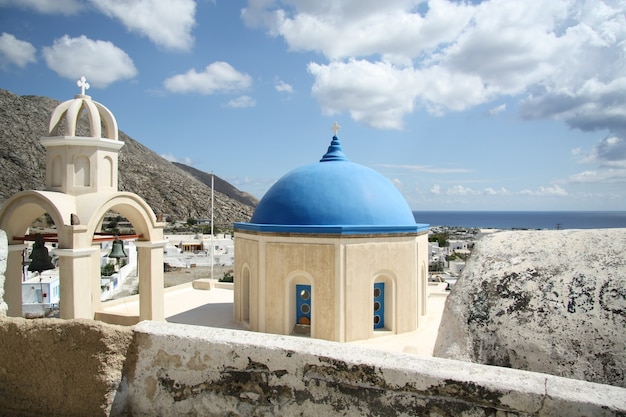 Kościół z niebieską kopułą pod słońcem i błękitnym pochmurnym niebem na Santorini, Grecja