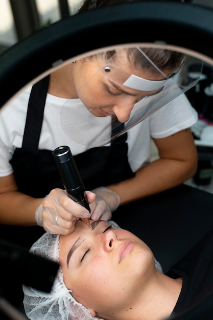 Kosmetyczka wykonująca zabieg microblading na kobiecie w salonie kosmetycznym