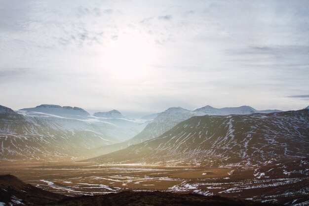 Krajobraz wzgórz pokryte trawą i śniegiem pod zachmurzonym niebem i światłem słonecznym w Islandii