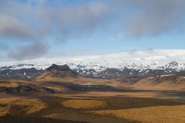 Krajobraz wzgórz pokrytych śniegiem pod zachmurzonym niebem i światłem słonecznym w Islandii