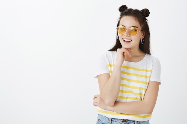 Kreatywna młoda kobieta pozuje z okularami przeciwsłonecznymi na białej ścianie