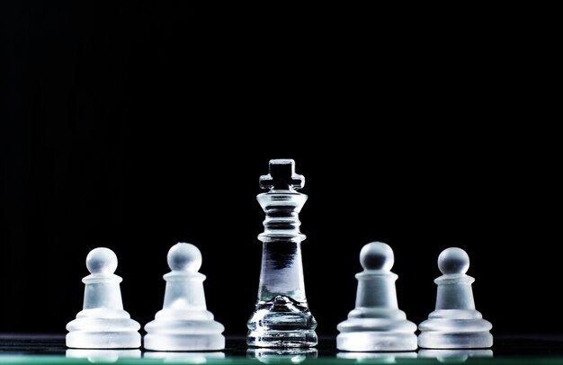 Król i kilka pionków na szachownicy na ciemnym tle. Koncepcja hierarchii.