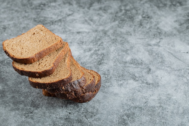 Kromki brązowego świeżego chleba na szarym tle.