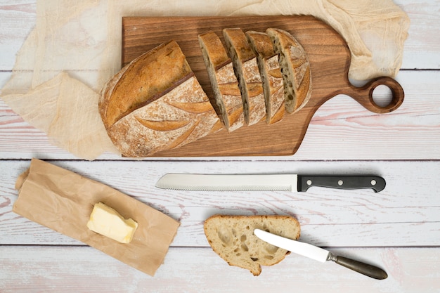 Kromki chleba; nóż; masło na papierze i nożyk na drewnianym stole