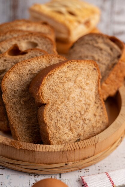 Kromki chleba umieszczone w drewnianym talerzu na białym drewnianym stole.