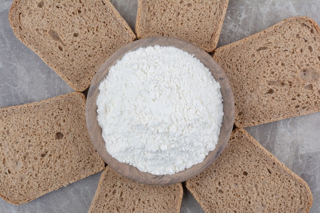 Bezpłatne zdjęcie kromki ciemnego chleba z mąką na marmurowej powierzchni