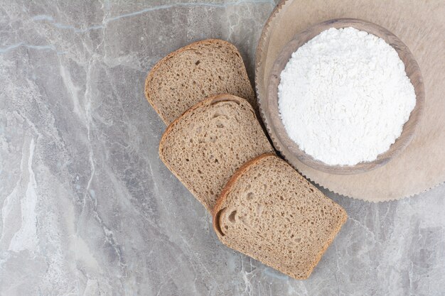 Kromki ciemnego chleba z mąką na marmurowej powierzchni