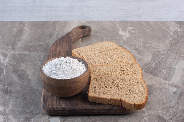 Kromki czarnego chleba i miskę mąki na desce na marmurowym tle. Zdjęcie wysokiej jakości