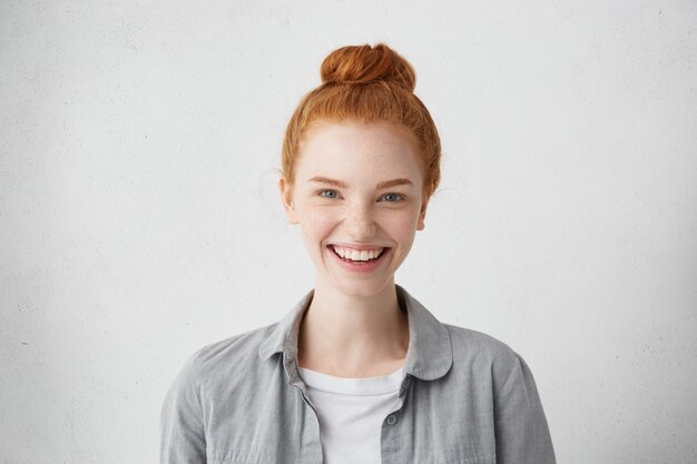 Kryty portret stylowej nastolatki z piegami i rudymi włosami kok patrząc na kamery z wesołym uśmiechem