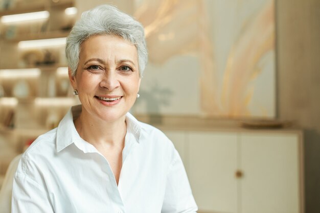 Kryty portret udanej bizneswoman w średnim wieku z krótkimi siwymi włosami, pracująca w swoim biurze