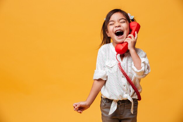 Krzyczy podekscytowany dziewczynka dziecko rozmawia przez czerwony telefon retro.