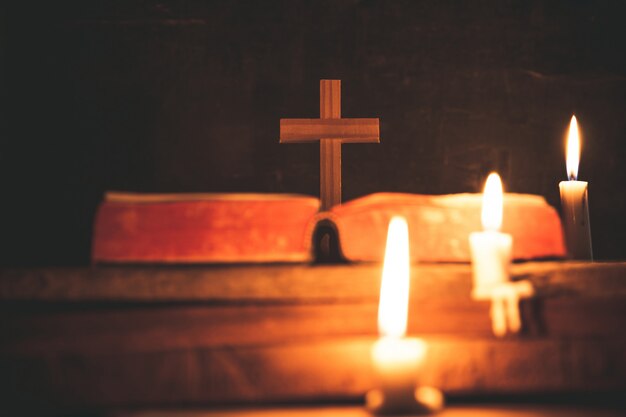 Krzyż z biblią i świeczką na starym drewnianym dębowym stole. Piękne złote tło.