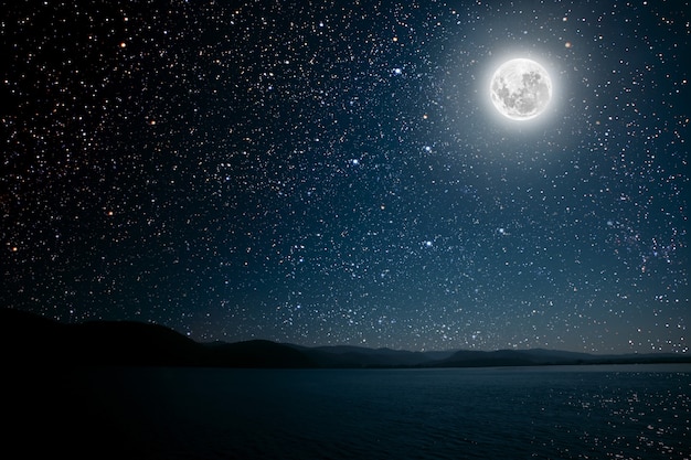 Księżyc na tle jasnego, gwiaździstego nieba odbitego w morzu.