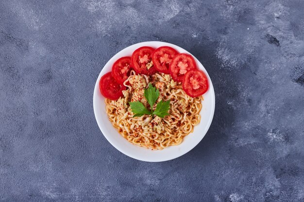 Kubek spaghetti z plastrami pomidora.