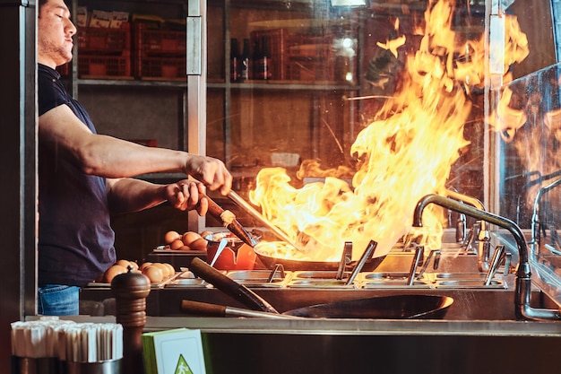 Kucharz smaży warzywa z przyprawami i sosem w woku na ogniu. Proces gotowania w azjatyckiej restauracji.
