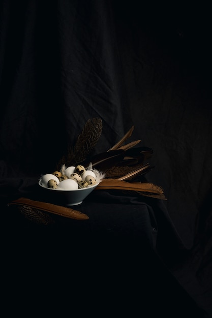 Bezpłatne zdjęcie kurczak i przepiórek jajka między piórkami w pucharze blisko dużych dutek