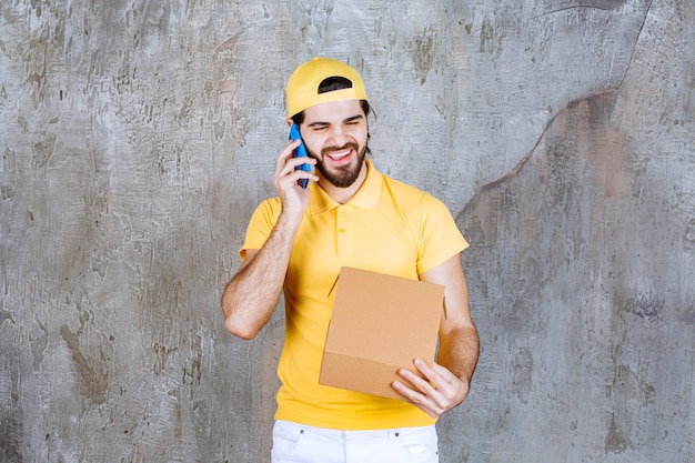 Bezpłatne zdjęcie kurier w żółtym mundurze trzymający otwarte kartonowe pudełko i przyjmujący zamówienia przez telefon
