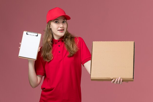 kurierka w czerwonym mundurze trzyma pudełko z jedzeniem i notatnik na różowym, jednolitym zleceniu dostawy usług
