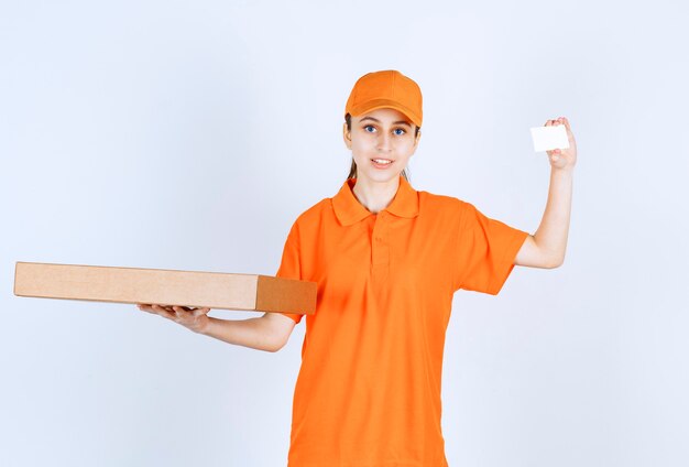 Kurierka w pomarańczowym mundurze trzyma pudełko po pizzy na wynos i prezentuje swoją wizytówkę.