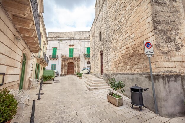 Kuszący widok na puste uliczki starego miasta Martina Franca z ładnymi domkami pomalowanymi na biało wśród zieleni. Cudowny dzień w miejscowości turystycznej, Apulia, Włochy.