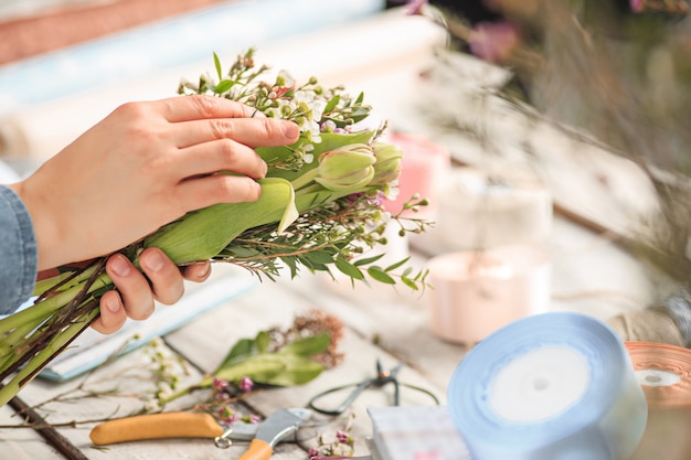 Kwiaciarnia w pracy: kobiece dłonie kobiety tworzącej nowoczesny bukiet różnych kwiatów