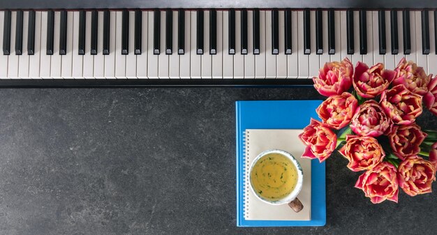 Bezpłatne zdjęcie kwiaty fortepianowe, notatki i filiżanka herbaty na ciemnym tle, widok z góry