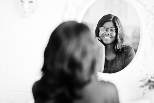 Ładna afroamerykanka w okularach postawiona w pokoju przed lustrem
